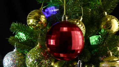 Kutudaki koyu kırmızı bir Noel topu, toplarla süslenmiş Noel ağacı dallarının arka planında dönüyor.