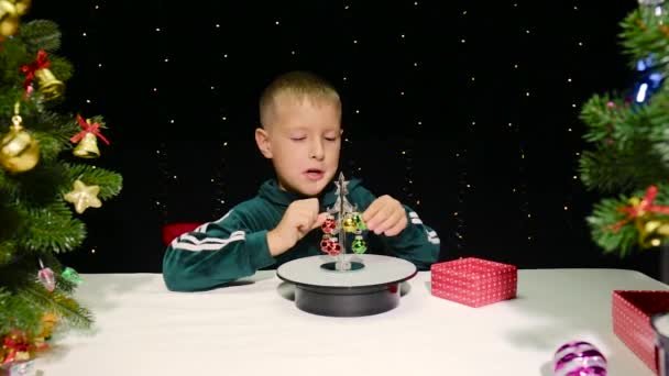 Ein Kleiner Junge Schmückt Einen Weihnachtsbaum Umgeben Von Geschmückten Weihnachtsbäumen — Stockvideo
