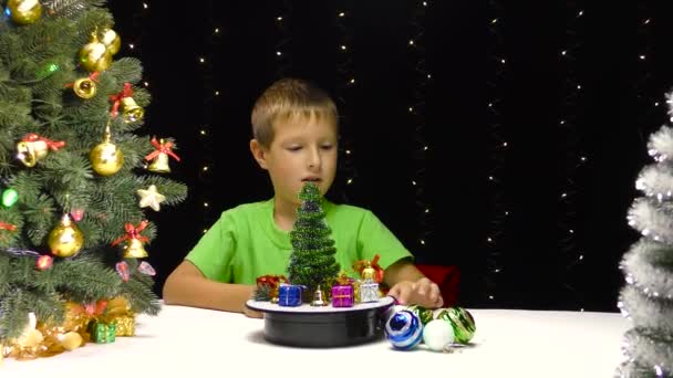 Niño Pone Decoraciones Navidad Una Superficie Giratoria Cerca Pequeño Árbol — Vídeos de Stock