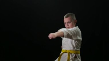 Sarı kuşak trenli şişman sporcu çocuk siyah arka plana yumruk atıyor.