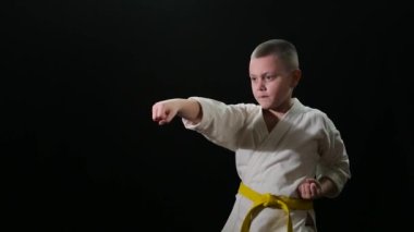 Sarı kuşak trenli şişman sporcu çocuk siyah arka plana yumruk atıyor.