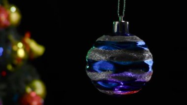 Siyah bir arka planda, süslenmiş bir Noel ağacının yanında gümüş çizgili mavi bir yeni yıl balosu dönüyor.