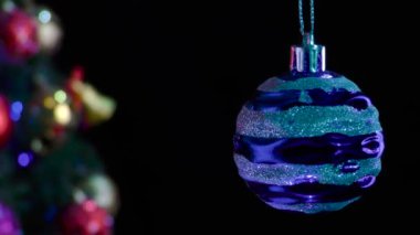 Siyah bir arka planda, gümüş çizgili mavi bir yeni yıl balosu süslemeli bir Noel ağacının yanında yavaşça döner.