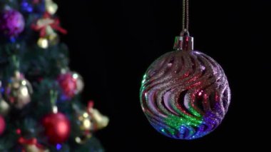 Siyah arka planda, gümüş çizgili pembe bir Noel balosu Noel ağacının yanında dönüyor.