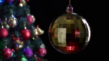 Siyah arka planda, sarı yanardöner bir Noel topu süslü bir Noel ağacının yanında döner.
