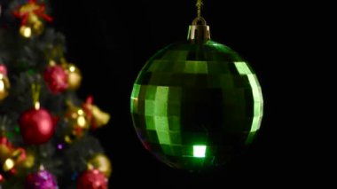 Siyah arka planda, parlak yeşil bir yılbaşı balosu süslü bir Noel ağacının yanında döner.
