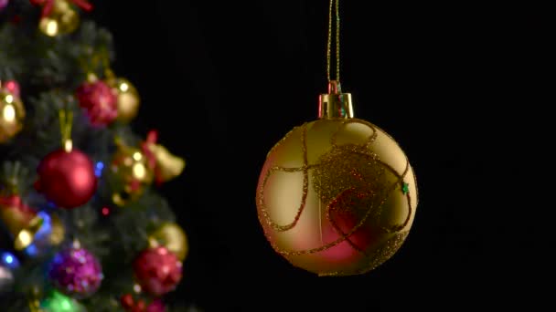 装飾されたクリスマスツリーの近くでパターンが回転する黄色いクリスマスボール — ストック動画