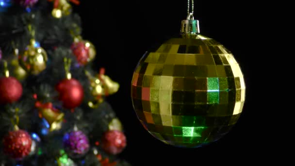 在黑色的背景上 一个黄色的圣诞球在一棵装饰过的圣诞树附近旋转 — 图库视频影像