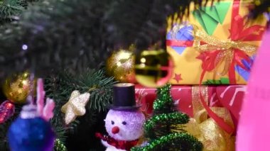 Küçük Noel ağaçlarının yanında dönen Noel ağacı süslemeleri ve hediye üzerinde duran bir kardan adam.