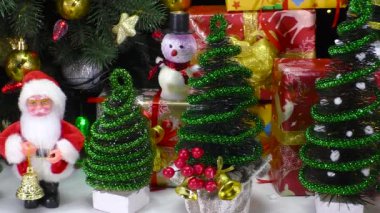 Noel Baba 'nın yakın çekimleri, hediyelerin yanında küçük süslü Noel ağaçları ve bir kardan adamla çevrili.