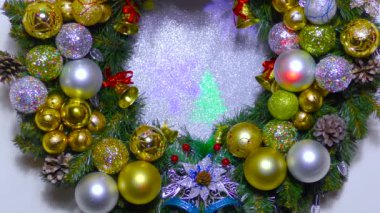Beyaz arka planda büyük bir Noel çelengi renkli toplar ve çanlar ile süslenmiş.