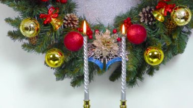 Yanan iki mumun arkasında hareketli bir Noel ağacı dalları kadar güzel bir Noel çelengi var.