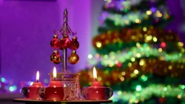 Noel ağacı ile yarı bulanık bir arka planda, yanan kırmızı mumlar arasında küçük toplarla süslenmiş küçük bir Noel ağacı dönüyor.