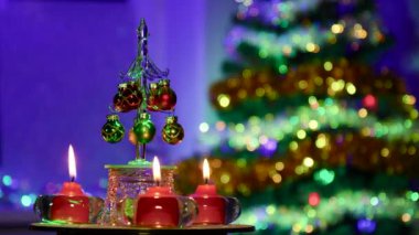 Noel ağacı ile yarı bulanık bir arka planda, yanan kırmızı mumlar arasında küçük toplarla süslenmiş küçük bir Noel ağacı dönüyor.
