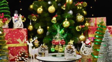 Bir Noel ağacı, büyük bir Noel ağacı ve Noel süslemelerinin yanında çam kozalaklarıyla çevrili bir tezgahta döner.