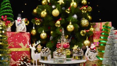 Bir Noel ağacı, büyük bir Noel ağacı ve Noel süslemelerinin yanında çam kozalaklarıyla çevrili bir tezgahta döner.