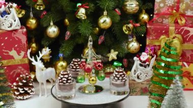 Bir Noel ağacı, büyük bir Noel ağacı ve hediyelerin yanında çam kozalaklarıyla çevrili bir tezgahta döner.