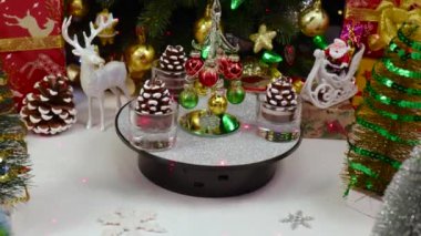 Büyük bir Noel ağacı ve hediyelerin yanında çam kozalağı şeklinde mumlarla çevrili bir Noel ağacı dönüyor.