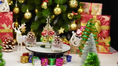 Bir Noel ağacı, büyük bir Noel ağacı ve Noel süslemelerinin yanında çam kozalağı şeklinde mumlarla çevrili bir tezgahta döner.