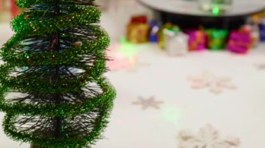 Küçük bir Noel ağacı, büyük bir Noel ağacının yanında çam kozalaklarıyla çevrili bir tezgahta döner.