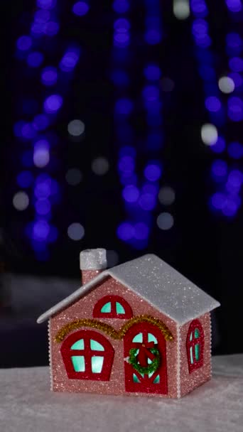 在一棵大圣诞树的背景下 有一幢浅棕色的圣诞别墅 房子的内部垂直地闪烁着蓝绿色的光芒 — 图库视频影像