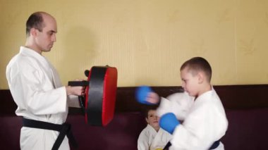 Elinde mavi pedleri olan bir çocuk antrenörün elindeki simülatöre yumruk atıyor.
