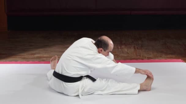 Athlete Black Belt Performs Bends Different Legs While Sitting Floor Stock Video