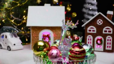 Bir geyik heykeli ve renkli Noel topları. Evlerin ve dekorasyonların yanında dönüyor.