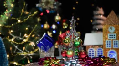 Küçük cam bir Noel ağacının ve renkli hediyelerin yakın plan çekimleri evlerin ve Noel ağaçlarının arka planında dönüyor.