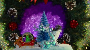 Noel figürleriyle çevrili mavi bir Noel ağacı bir Advent çelenginin arka planında dönüyor