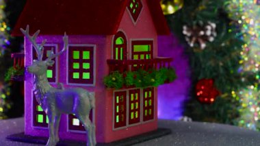 Yanında biblolar olan pembe bir Noel süslemeli ev dekore edilmiş bir Noel çelenginin arka planında dönüyor.