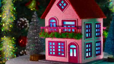 Noel ağaçlarıyla çevrili dekore edilmiş iki katlı bir ev, bir Noel çelenginin arka planında dönüyor.