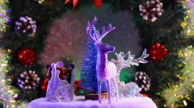 Noel Baba 'nın kızakla çevirdiği mavi bir Noel ağacının yakın çekimi ve süslenmiş bir Noel çelenginin arka planında dönen ren geyiği.