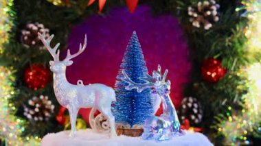 Noel Baba 'nın kızakla çevirdiği mavi bir Noel ağacının yakın çekimi ve Noel çelenginin arka planında dönen ren geyiği.