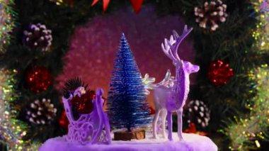 Noel Baba 'nın kızakla çevirdiği mavi bir Noel ağacı ve süslü bir Noel çelenginin arka planında dönen ren geyiği.