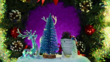 Noel Baba 'nın kızakla çevirdiği mavi bir Noel ağacı ve bir Noel çelenginin arka planında dönen ren geyiği.
