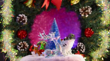 Noel ağacının etrafı Noel Baba 'nın kızağıyla çevrili, bir geyik ve bir kızakla cam top bir Noel çelenginin arka planında dönüyor.