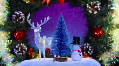 Noel geyiği kardan adam ve köknar ağacı süslü bir Noel çelenginin arka planında dönerler.