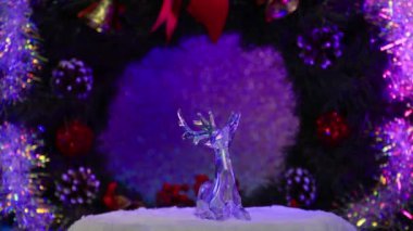 Bir geyiğin cam heykeli, bir Noel çelenginin arka planında döner.
