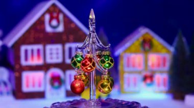 Toplarla süslenmiş küçük bir Noel ağacı Noel evlerinin arka planında dönüyor.