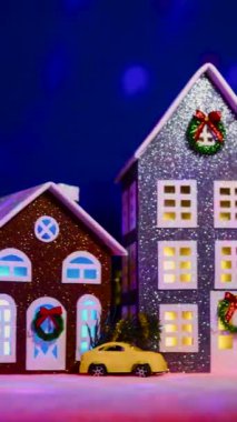 Süslü renkli evleri olan, koyu mavi arka planda uçan animasyonlu bir Noel kasabası.