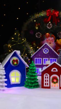 Hareketli büyük sihirli bir Noel kasabası. Yanında renkli evler ve küçük renkli Noel ağaçları var. Siyah arka planda yanıp sönen ışıklar var.