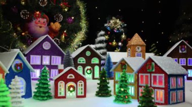 Pencerelerinde ışıklar ve yanında küçük renkli Noel ağaçları olan renkli güzel evleri olan sihirli bir Noel kasabası.