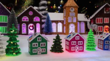 Süslü çatıları ve büyük bir Noel kasabasının arka planında yan yana duran üç küçük Noel evi.
