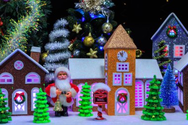Noel kasabası, evlerin camlarında kırmızı mor ve pembe ışıklar var. Noel Baba ve farklı boyutlarda Noel ağaçları var.