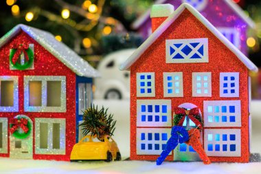 Turuncu ve kırmızı renkli evlerin yakın plan fotoğrafları. Bir Noel kasabasının arka planında arabaları ve anahtarları var.