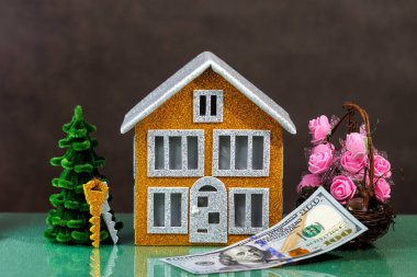 Kahverengi ev, içinde anahtarlar, çiçekler ve yüz dolarlık banknotlar olan bir Noel ağacı ile çevrilidir.