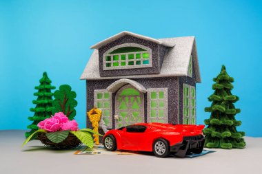 Çiçeklerle çevrili gri bir ev ve yeşil ışık ve avro banknotunun üzerinde duran kırmızı bir araba.