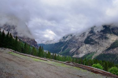 Kayalık dağların üzerinde alçak bulutlarla dolu uzun bir vadiyi görmek