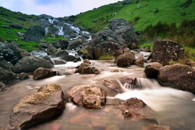 Stream running off the hilside into a stone lined pool clipart